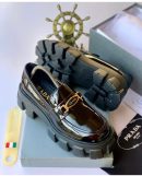 Black patent leather Prada penny loafers with chunky grey lug sole and gold hardware - luxury men's designer shoes.