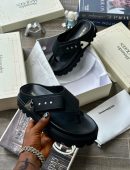 Black and olive green Alexander McQueen leather thong sandals with chunky platform sole and buckle detail displayed on boxes.