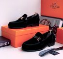 Black velvet loafers with gold metal hardware bit displayed with orange Hermès box and shoe horn.