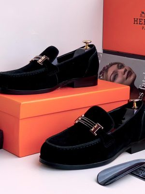Black velvet loafers with gold metal hardware bit displayed with orange Hermès box and shoe horn.