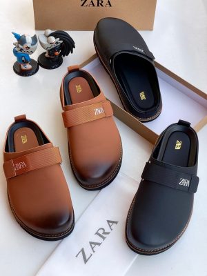 ZARA men’s slip-on mules in brown gradient and black with branded elastic strap and chunky stitched sole, displayed beside branded box and figurines on white background.