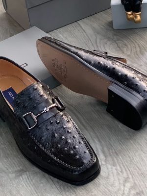 Men's brown genuine ostrich leather horsebit loafers with square toe and rubber sole, displayed on grey wood floor with branded shoebox.