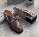 Men's brown genuine ostrich leather horsebit loafers with square toe and rubber sole, displayed on grey wood floor with branded shoebox.