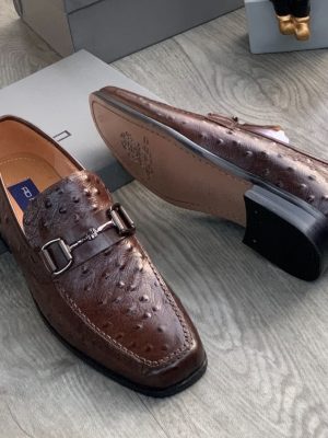 Men's brown genuine ostrich leather horsebit loafers with square toe and rubber sole, displayed on grey wood floor with branded shoebox.