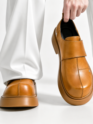 Men's luxury leather monk-strap loafers with chunky black platform soles and silver hardware accents being held by hand next to white trousers.
