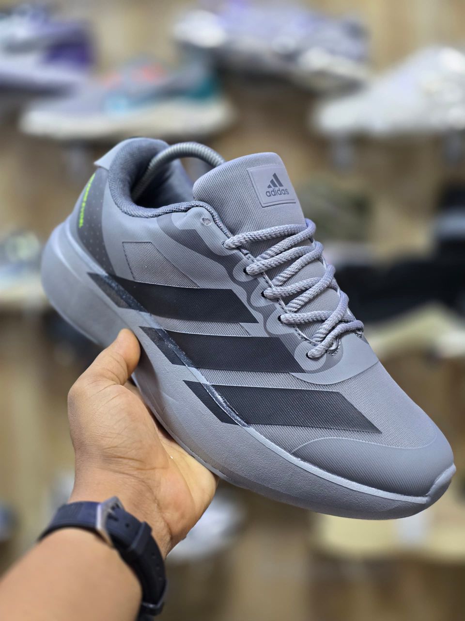 Adidas Men’s Luxury Comfort Sneakers A pair of men's luxury black comfort sneakers with grey accents, displayed on a blue box with a hand holding one shoe, showcasing their bold design and thick, cushioned sole.
