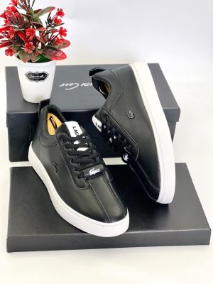 A pair of men's luxury black leather sneakers with a white sole, displayed on a black box with a decorative plant, showcasing their sleek design and premium material.