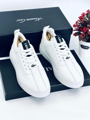 A pair of men's luxury black leather sneakers with a white sole, displayed on a black box with a decorative plant, showcasing their sleek design and premium material.