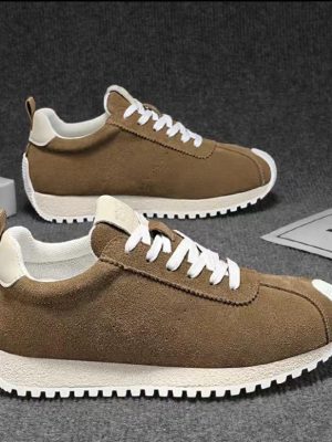 A pair of men's luxury brown suede sneakers with white laces and a white ridged sole, displayed on a grey textured surface, showcasing their classic design and premium material.