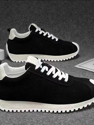 A pair of men's luxury brown suede sneakers with white laces and a white ridged sole, displayed on a grey textured surface, showcasing their classic design and premium material.