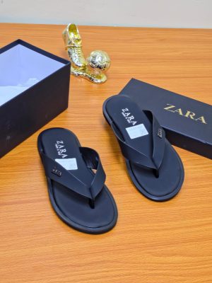 A pair of men's luxury white leather sandals with a brown sole, displayed on a wooden surface next to a black shoebox, showcasing their premium material and elegant design.