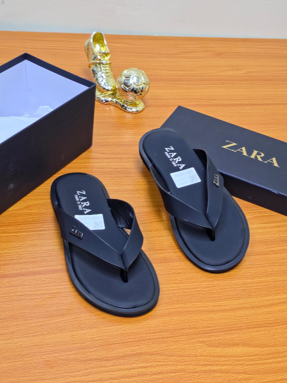Men’s Luxury Leather Slide A pair of men's luxury white leather sandals with a brown sole, displayed on a wooden surface next to a black shoebox, showcasing their premium material and elegant design.
