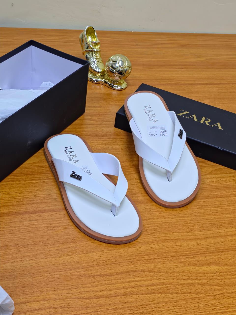 Men’s Luxury Leather Slide A pair of men's luxury white leather sandals with a brown sole, displayed on a wooden surface next to a black shoebox, showcasing their premium material and elegant design.