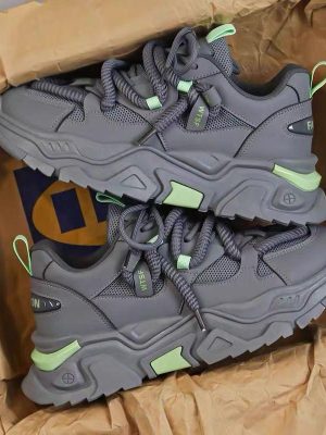 A pair of men's luxury grey chunky sneakers with lime green accents, displayed in a box with brown paper, showcasing their bold design and thick, cushioned sole.