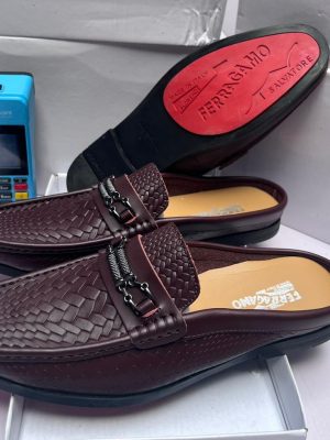 Salvatore Ferragamo brown perforated leather loafer with Gancini bit buckle, held by hand showcasing craftsmanship