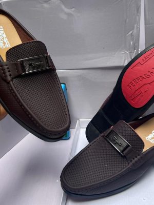 Salvatore Ferragamo brown perforated leather loafer with Gancini bit buckle, held by hand showcasing craftsmanship