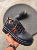Black leather luxury sneakers with chunky platform sole and distinctive orange geometric charm - men's designer streetwear shoes.