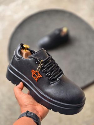 Black leather luxury sneakers with chunky platform sole and distinctive orange geometric charm - men's designer streetwear shoes.