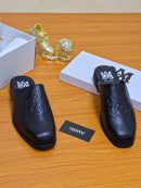 Black Amiri leather slides with embossed logo displayed on a wooden table with white packaging and gold decor.