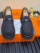 Black Hermès woven leather loafers with gunmetal horsebit hardware and chunky platform sole displayed in signature orange Hermès box with gold decorative pieces