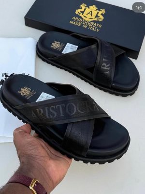 Black Aristocrats Luxury cross-strap slides with rugged sole and Made in Italy branding displayed with black box and dust bag.