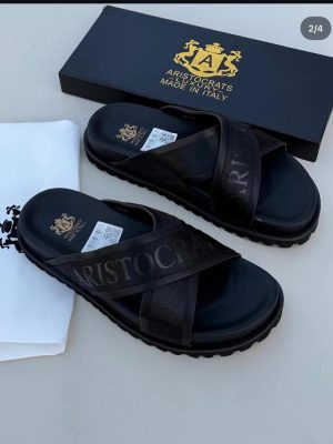Black Aristocrats Luxury cross-strap slides with rugged sole and Made in Italy branding displayed with black box and dust bag.