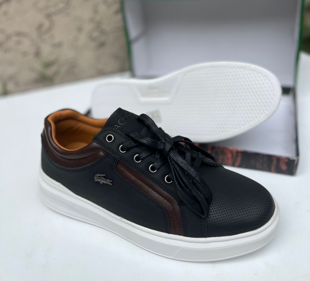 Premium Lacoste leather sneakers Black Lacoste leather sneakers with brown accents and white sole displayed with shoe box.