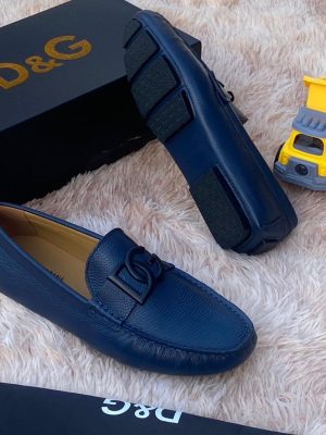 Navy blue D&G pebbled leather driving loafers with black hardware and rubber sole displayed on fluffy rug with D&G box and toy truck.