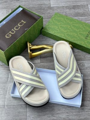 Gucci men's black and white Web stripe slide sandals with rubber footbed, displayed with green Gucci box and gold decorative item on wooden floor.