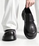 Men's luxury black leather monk-strap loafers with chunky black platform soles and silver hardware accents being held by hand next to white trousers.