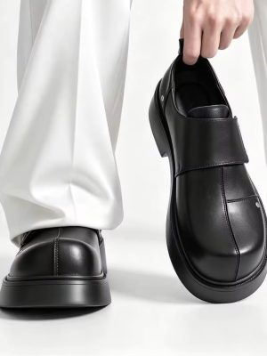 Men's luxury black leather monk-strap loafers with chunky black platform soles and silver hardware accents being held by hand next to white trousers.