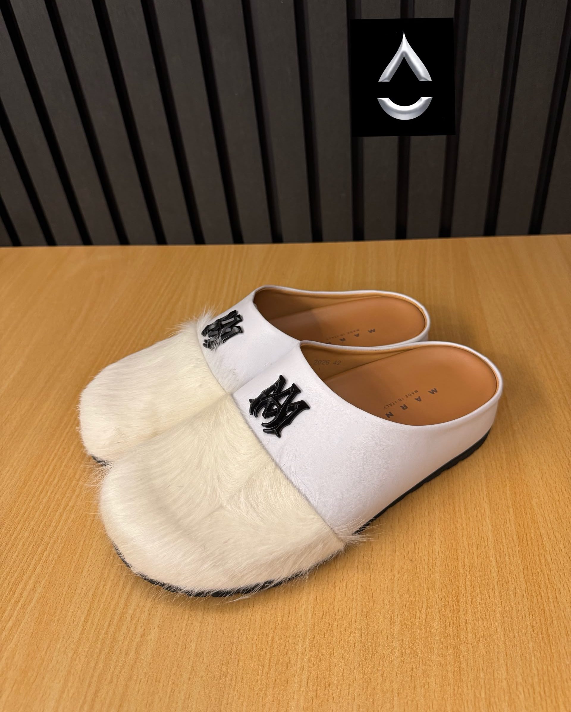 Iconic AMIRI fur-detailed slide mules AMIRI luxury fur slide mules in white, black, and brown with authentic leather upper, plush fur detailing, signature AM logo, and cushioned sole displayed with original black AMIRI box