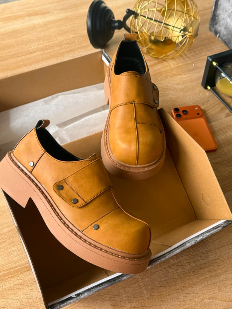Premium leather monk-strap loafers Men's luxury leather monk-strap loafers with chunky black platform soles and silver hardware accents being held by hand next to white trousers.
