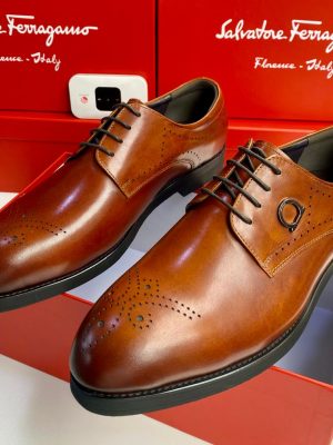 Men's tan Salvatore Ferragamo leather brogue oxfords with Gancini hardware and rubber sole, displayed with branded red shoeboxes on white surface.
