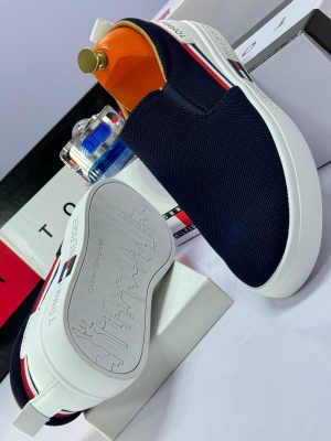 Alt Text: Black knit Tommy Hilfiger slip-on sneakers with white platform sole and red, white, blue flag stripe - luxury men's casual shoes.