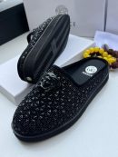 Versace men’s black studded slip-on mules with Medusa head hardware and chunky platform sole, displayed beside branded box and beaded bracelet on white background.