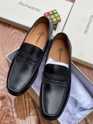 Richwanaz men’s brown leather penny loafers with burnished finish and hand-stitched toe, displayed beside branded box on wooden surface.