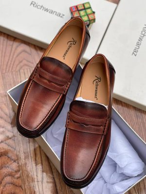 Richwanaz men’s brown leather penny loafers with burnished finish and hand-stitched toe, displayed beside branded box on wooden surface.