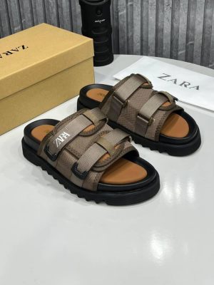 Zara men's taupe tactical slide sandals with double adjustable straps, white logo branding, and chunky black rubber lug sole, displayed with branded box and dust bag on white surface.