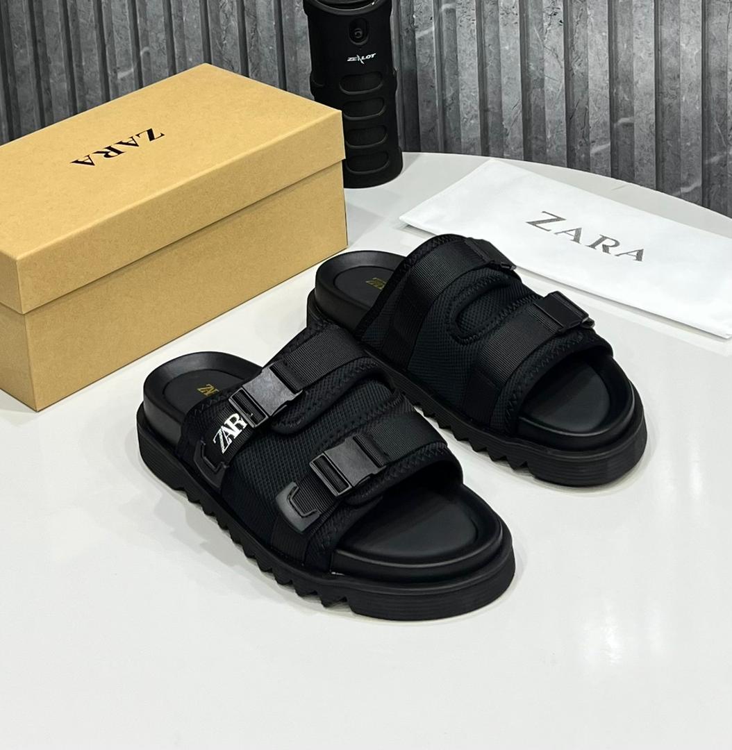 Premium Zara tactical slide sandals Zara men's taupe tactical slide sandals with double adjustable straps, white logo branding, and chunky black rubber lug sole, displayed with branded box and dust bag on white surface.