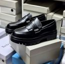 Men's luxury black leather fringed loafers with chunky black lug soles and silver hardware accents resting on white shoeboxes.