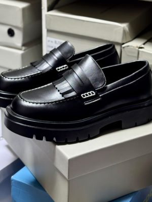Men's luxury black leather fringed loafers with chunky black lug soles and silver hardware accents resting on white shoeboxes.
