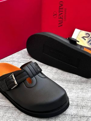 Black leather Valentino Garavani slides with buckle strap detail, orange footbed, and chunky black sole - luxury men's sandals