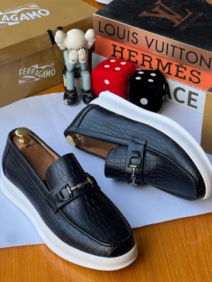 Black crocodile-embossed leather loafers with horsebit metal hardware and white platform sole displayed with luxury brand boxes