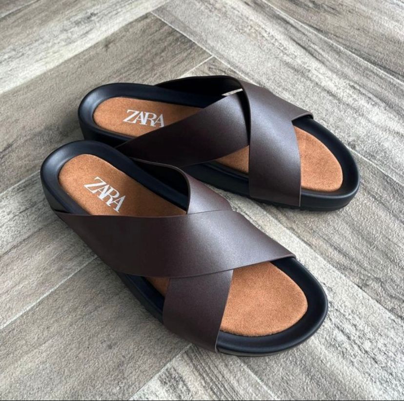 Sleek ZARA black cross-strap slides Black ZARA cross-strap slides with cork footbed and branded insole on wooden floor background