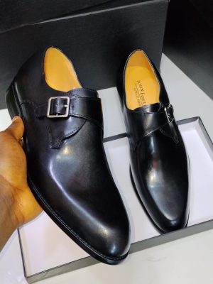 Black leather John Foster single monk strap dress shoes with silver buckle and tan lining displayed in box.