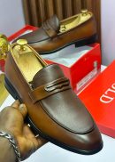 Brown two-tone leather loafers with pebbled texture and metal bit hardware held in hand, displayed with red shoe box.