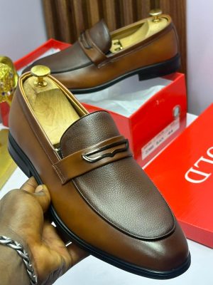 Brown two-tone leather loafers with pebbled texture and metal bit hardware held in hand, displayed with red shoe box.
