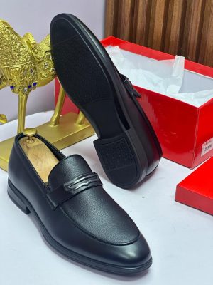 Brown two-tone leather loafers with pebbled texture and metal bit hardware held in hand, displayed with red shoe box.