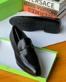 Black Clarks leather loafers with metal chain-bit hardware displayed in green Clarks box with luxury brand books.
